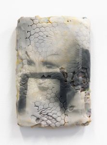 Porous, black an white sculpture with an image of a face.