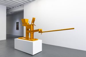 Yellow sculpture with long protruding moveable arm.