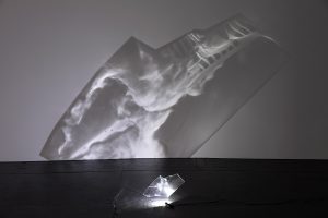 Light illuminates a piece of plexiglass, casting an image on the wall.