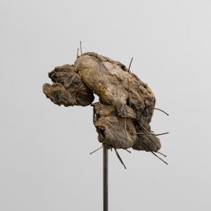 Flattened piece of bread casted in bronze, suspended in the air on a tall slender stand. Wire or spores grow out of the bronze loaf.