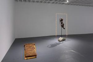 "Gallery view close up to the large tabloid on the floor, and the figure withs lights framing it in the back. "