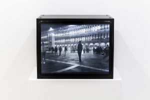 Black box tv with an iamge of a man standing in a busy street at night.