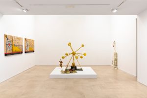 Gallery view from left to right, two works hang on the wall, one large work stands in the canter, on work stands in the back corner.