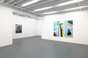 Gallery view of two walls with one work on each: black and white abstract composition on left and abstract multicolor composition on right
