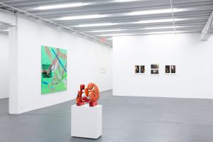 Gallery view from left to right: bright green painting, red sculpture, and framed photographs on wall