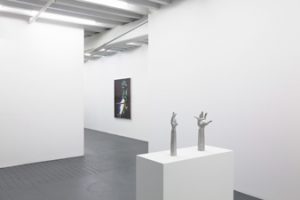 Gallery view of group exhibition "Regroup" at Miguel Abreu Gallery. From left to right is Eileen Quinlan's digital chromogenic black print "Scam Likely" and Jean-Luc Moulene's printed aluminum sculpture "Hands Off (Paris 2019)," a silver sculpture of two arms and hands pointing upwards placed on a white pedestal.