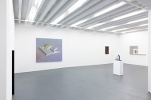 Gallery view of group exhibition "Regroup" at Miguel Abreu Gallery. From left to right is Cameron Rowland's "U60" skinny, black rod sculpture attached to the wall, Dana Lok's oil painting titled "Weather System" portraying a gray and purple painting of an open book with a rainbow coming out of it, Matthew Ronay's small blue and yellow sculpture titled "Eight Tissues One Hand," R.H Quaytman's maroon colored painting "Silhouette" and R.H Quaytman and Moyra Davey's grey colored print, "Mothers of Men, Chapter 33."