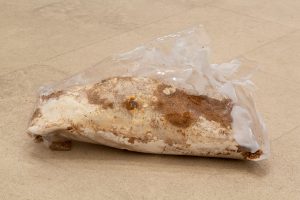 Brown and white earthy material wrapped in clear, white plastic sheet