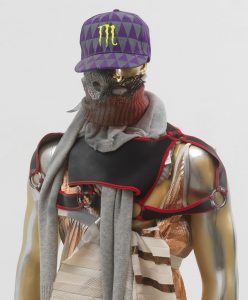 Gold and silver spray painted mannequin wearing cap, masquerade mask, and various clothing items