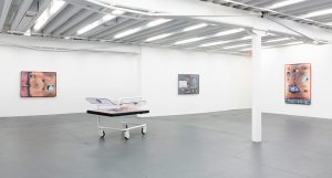 Gallery installation view, a sculpture standing on the floor with three works on separate walls behind it.