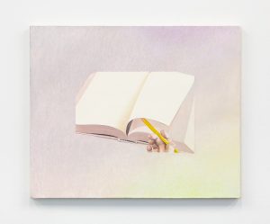 A hand turns the page of a book with a pencil.