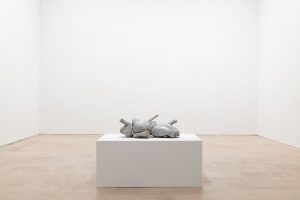 Concrete figure lying on a white pedestal in an empty space.
